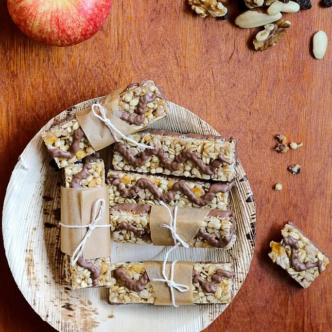 Homemade snack bars wrapped in paper on a plate, with nuts and apples