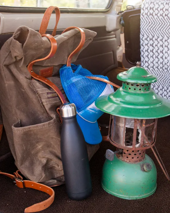 A waxed canvas rucksack, a steel flask and a green camping lantern packed in a car boot