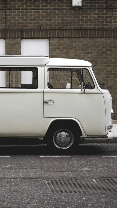 The front of a clean white VW camper van parked against a brick wall