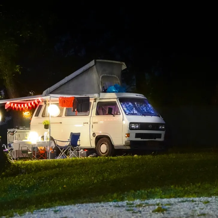 A camper van with its awning out at a campsite at night