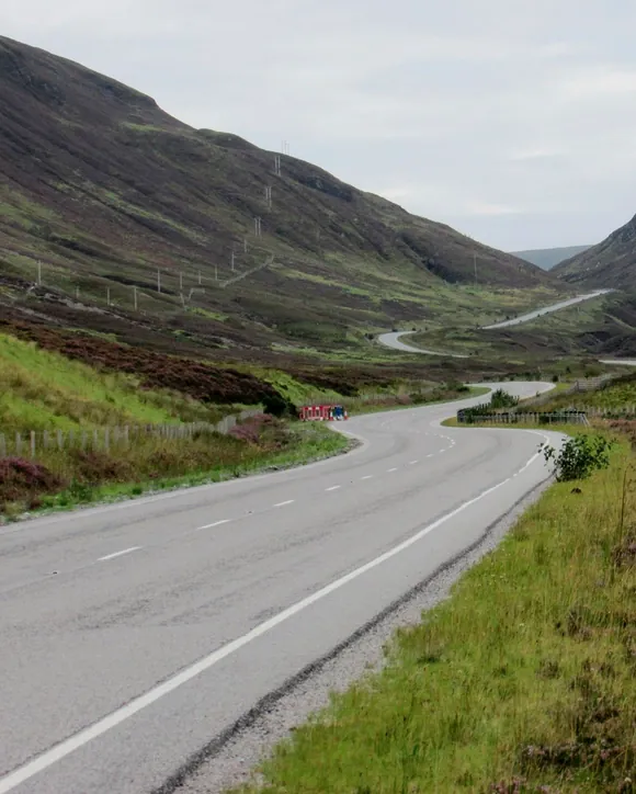 A road winding through a heather-covered glen in the Scottish Highlands